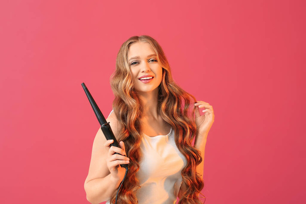 Hermosa mujer joven con rizador para el cabello contra el fondo de color - Foto, Imagen