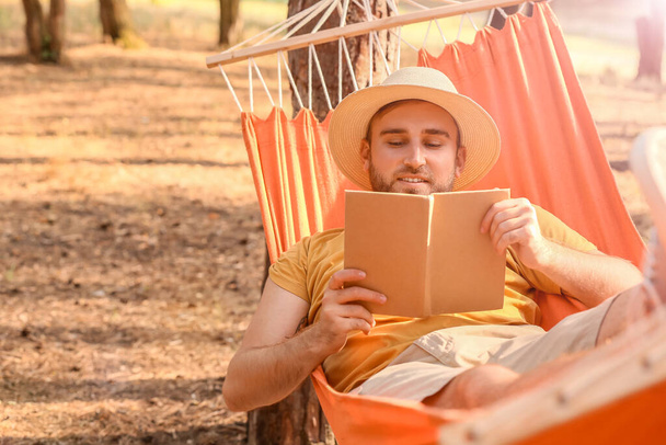 Jovem com livro relaxante em rede ao ar livre
 - Foto, Imagem