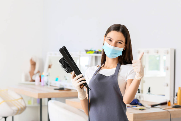 Счастливая женщина-парикмахер в медицинской маске в салоне во время эпидемии коронавируса - Фото, изображение