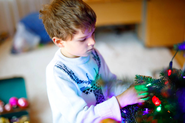 Krásný chlapec a barevné vintage vánočních hraček a míčků ve starém kufříku. Malé dítě, školák ve svátečních šatech zdobí vánoční stromek. Dítě se usmívá do kamery. Rodinná dovolená - Fotografie, Obrázek