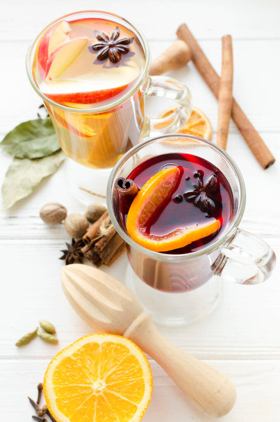 Two glasses of different type of mulled wine or gluhwein based on red and white wine with spices and ingredients on white wooden background. Spicy warm beverage. Hot seasonal mulled drink. - Φωτογραφία, εικόνα