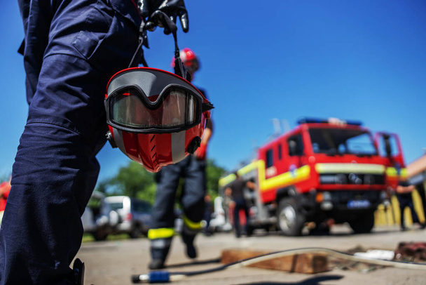 Detailní záběr hasiče držícího helmu a kráčejícího směrem k hasičskému vozu. - Fotografie, Obrázek