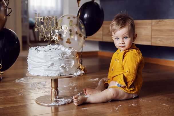 Mignon petit garçon assis sur le sol, fracassant et jouant avec son gâteau à son premier anniversaire. - Photo, image