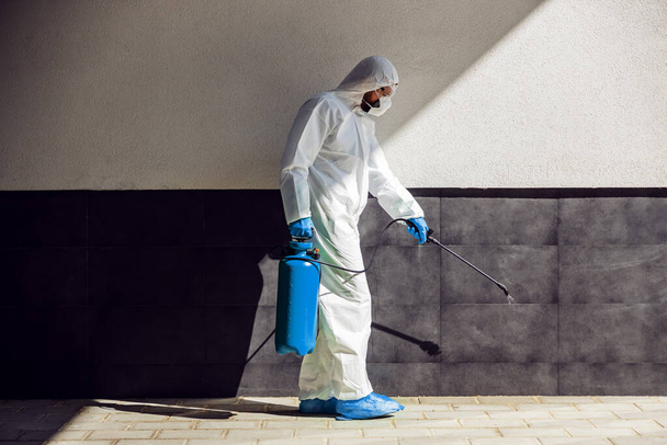 Comprimento total do homem em uniforme estéril e máscara esterilizando a superfície ao ar livre do vírus corona, fungo e doença. - Foto, Imagem