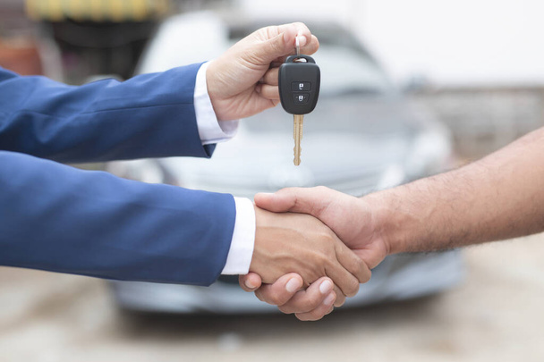 Close up of dealer giving key to new owner and shaking hands in auto show.auto business, car sale, deal,concept - Photo, Image