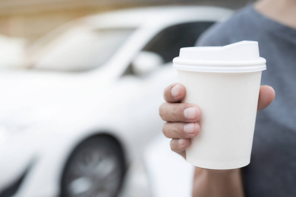 Женщина держит в руке горячий бумажный кофе, стоя в машине на боку перед тем, как сесть за руль автомобиля под утренним солнечным светом. транспорт и концепция транспортного средства. - Фото, изображение