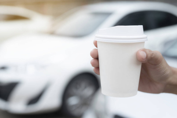 Женщина держит в руке горячий бумажный кофе, стоя в машине на боку перед тем, как сесть за руль автомобиля под утренним солнечным светом. транспорт и концепция транспортного средства. - Фото, изображение