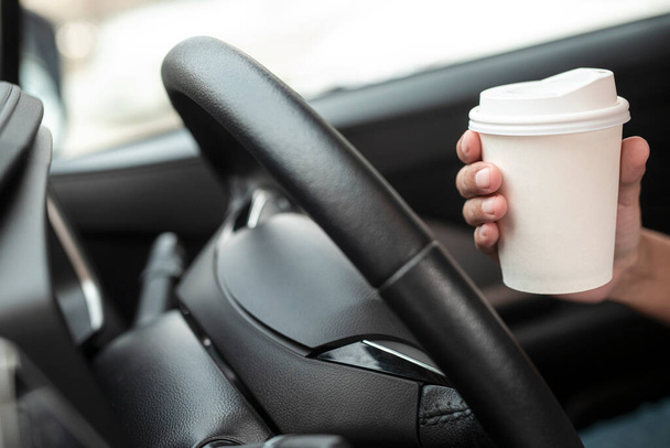 Женщина держит чашку горячего кофе в руке, сидя в машине перед вождением автомобиля под утренним солнечным светом. транспорт и концепция транспортного средства. - Фото, изображение
