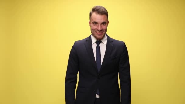 excited elegant young man in suit, looking up, rising eyebrows and laughing, holding hands and making thumbs up sign, celebrating victory and smiling on yellow background - Footage, Video