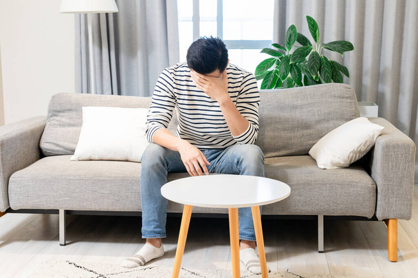 Asian man feel depressed and sitting on sofa at home  - Фото, изображение