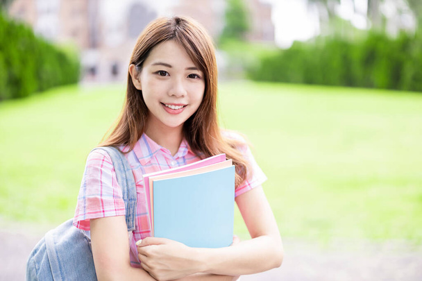 Asian college student smile to you with books holding in hands on campus - Photo, Image