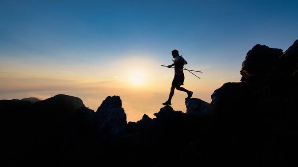 Silueta del atardecer del hombre del skyrunner que desciende de la cresta alpina con postes - Foto, Imagen