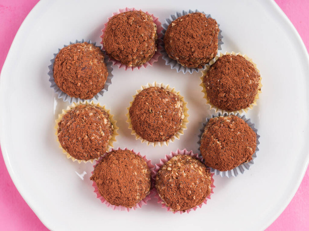 Home made vegan energy protein balls with oats, nuts, almond butter, dates, dried fruit, flax seeds, chocolate nibs on white dish on pink wooden background. Top view - Фото, изображение