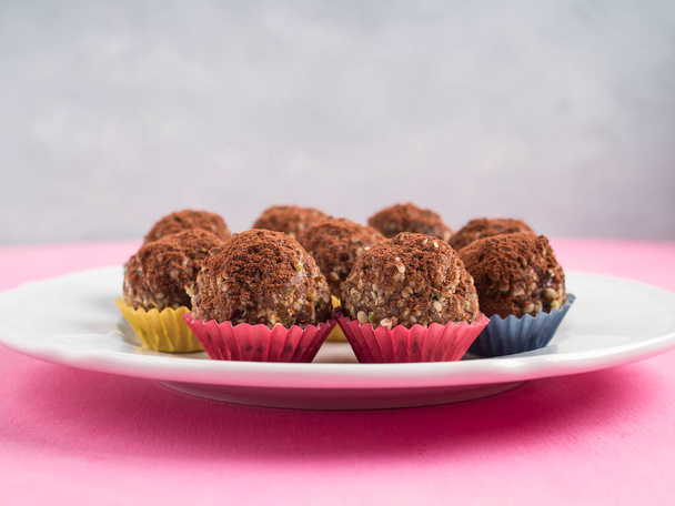 Home made vegan energy protein balls with oats, nuts, almond butter, dates, dried fruit, flax seeds, chocolate nibs on white dish on pink wooden background. Closeup - Φωτογραφία, εικόνα