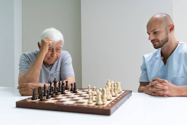 Yaşlı bunak evde bakıcı ile satranç oynuyor. - Fotoğraf, Görsel