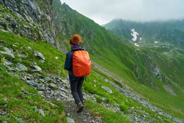 Female tourist with backpack hiking on a trail in the mountains - Фото, зображення