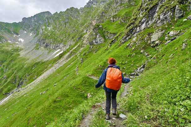 Female tourist with backpack hiking on a trail in the mountains - Fotoğraf, Görsel