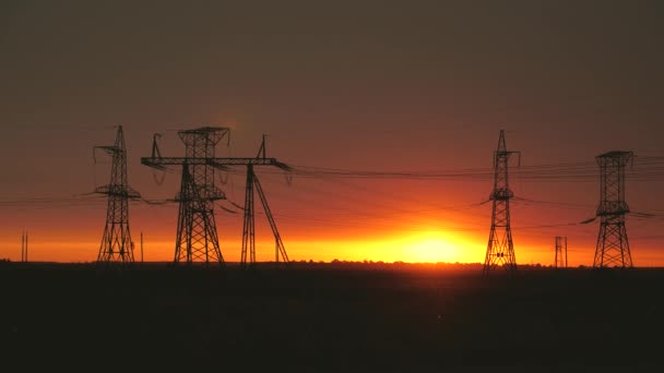 Wysokonapięciowe linie elektryczne w polu o zachodzie słońca. Ciemna sylwetka wież w promieniach pięknego wieczornego słońca. Dystrybucja i dostawa energii elektrycznej. czysta energia - Materiał filmowy, wideo