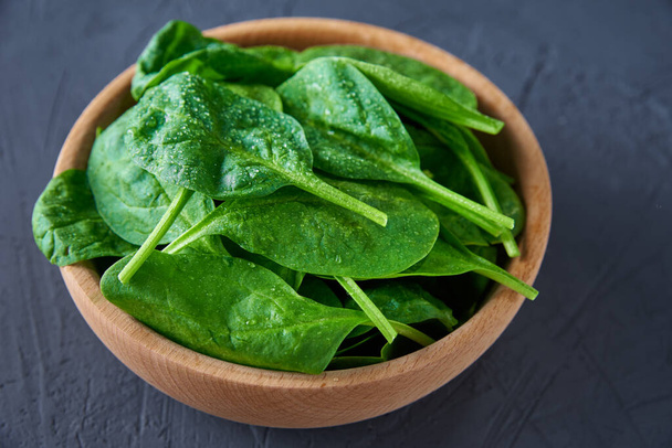 Fresh spinach leaves in wooden bowl on a dark background. Organic food - Photo, Image