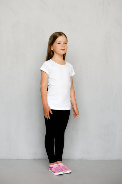 Cute young child with long hair in white t-shirt and black sweatpants posing  - Foto, Bild