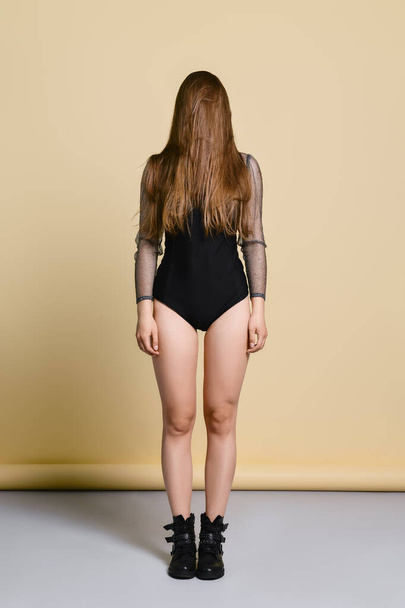 young woman in thight body suit and rough boots standing straight with hair on face in studio  - Foto, immagini