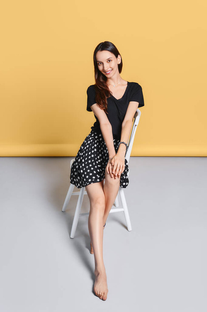 Beautiful happy young woman without make up sits on chair in studio on yellow background - Zdjęcie, obraz