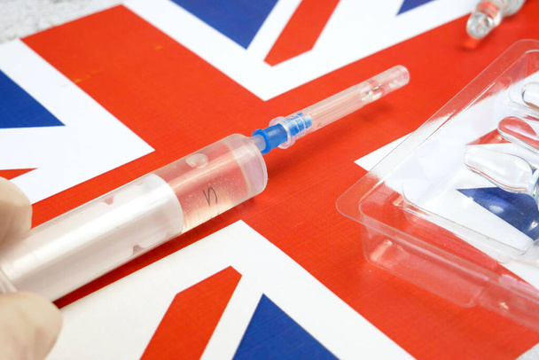 ruiskua rokotteella pidetään käsin käsineessä Englannin lipun alla, rokote koronavirusta vastaan, operaatio Poimunopeus, AstraZeneca-rokote - Valokuva, kuva