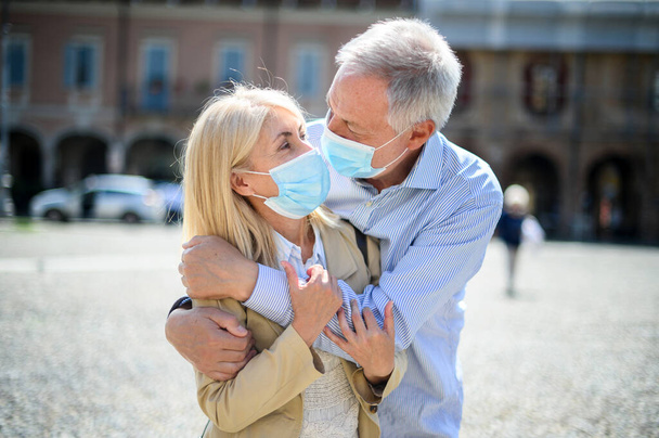 Love in the time of Coronavirus. Senior couple hugging outdoor wearing masks - 写真・画像