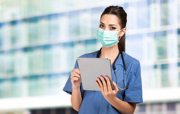 Masked young nurse doctor using a tablet - 写真・画像