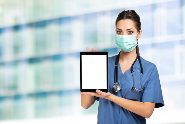 Masked nurse doctor showing a tablet with a white screen - Photo, image
