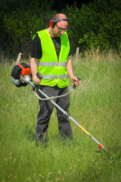 Працівник косить траву з тримером трави
 - Фото, зображення