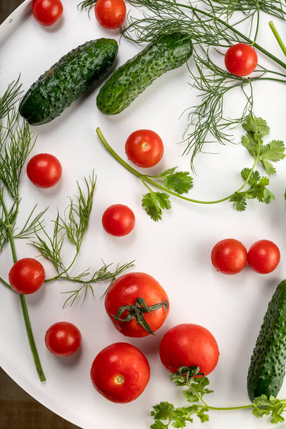 Fresh cucumbers and tomatoes with herbs with water drops on a round white background. - Foto, imagen