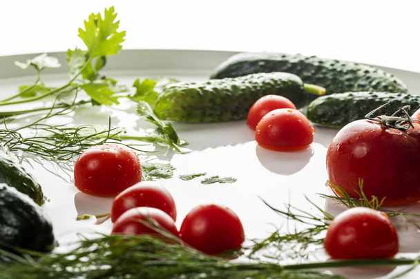 Verse komkommers en tomaten met kruiden met waterdruppels op een ronde witte achtergrond. - Foto, afbeelding
