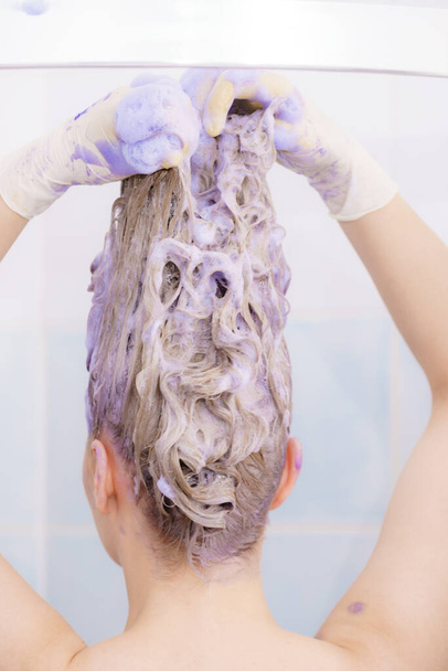 Woman applying coloring shampoo on her hair. Female having purple washing product. Toning blonde color at home. - Valokuva, kuva