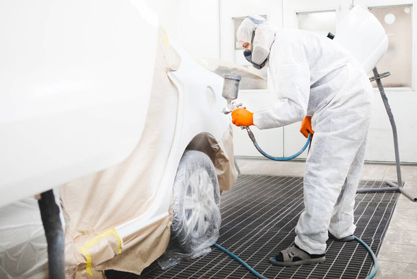 Professional male car painter is painting in garage by airbrush. Man works with spray gun. - Fotoğraf, Görsel