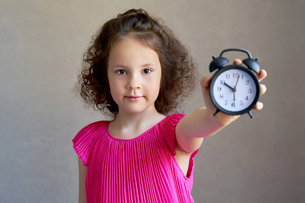 beautiful curly little girl with a Desk clock. - Fotoğraf, Görsel