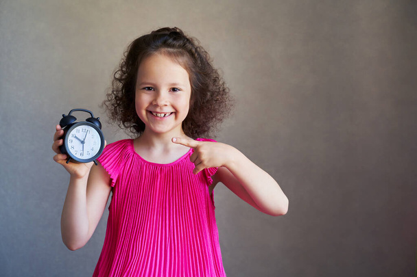 beautiful curly little girl with a Desk clock. - Foto, afbeelding