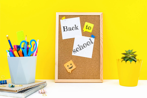 Vertically board for notes with wooden frame, the words Back to school on attached sticky sheets, office supplies and plant on table in classroom. Education, knowledge concept on a yellow background. - Foto, Imagem