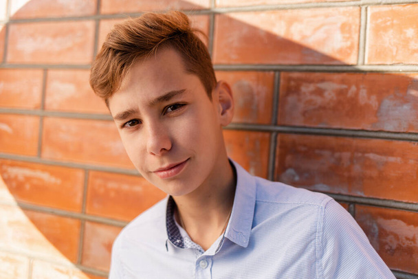 Egy fiatal tinédzser fiú portréja ingben, egy vörös téglafalnak támasztva.. - Fotó, kép
