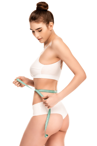 mujer joven con un cuerpo perfecto que mide la cintura aislada en blanco  - Foto, Imagen