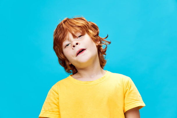O menino ruivo inclinou a cabeça para o lado contra um fundo azul
 - Foto, Imagem