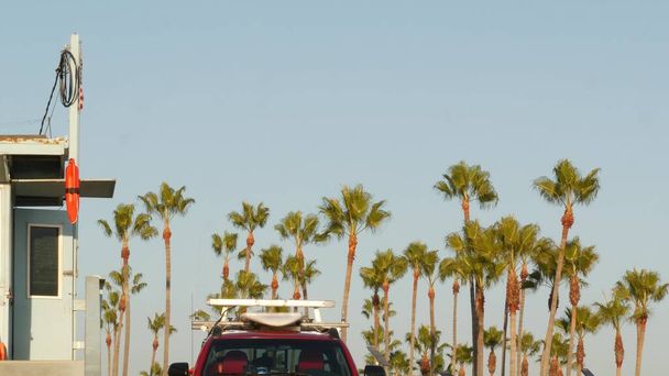 Iconische retro houten strandwacht toren, baywatch rode auto. Levensboei, Amerikaanse staatsvlag en palmbomen tegen de blauwe lucht. Summertime california esthetic, Santa Monica beach, Los Angeles, CA Verenigde Staten. - Foto, afbeelding