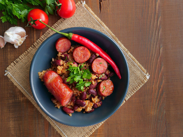 Feijão vermelho e arroz com salsicha em tigela sobre mesa de madeira
 - Foto, Imagem