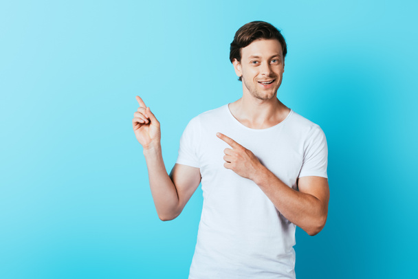 Hombre en camiseta blanca señalando con los dedos sobre fondo azul - Foto, imagen