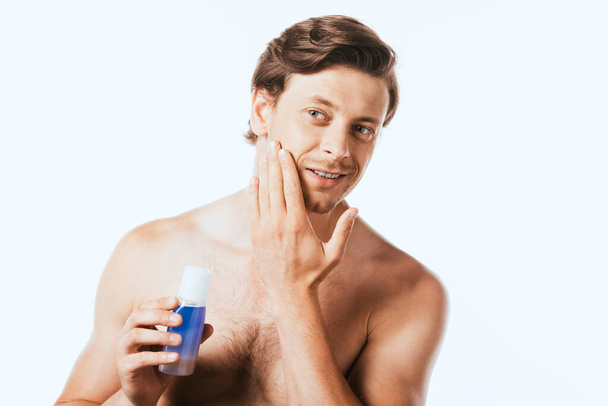 Shirtless man touching skin while holding bottle of toner isolated on white - Foto, Imagen