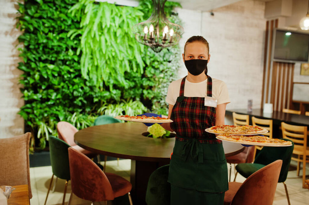 Waiter in protective mask hold pizza in pizzeria. - Photo, Image