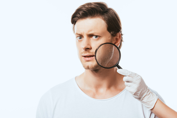 Dermatólogo sosteniendo lupa cerca de hombre pensativo aislado en blanco - Foto, Imagen