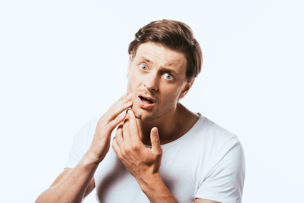Shocked man touching skin on cheek and looking at camera isolated on white - Fotoğraf, Görsel