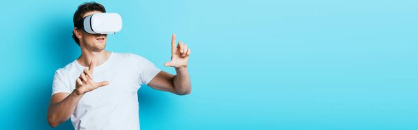 Horizontal crop of man in vr headset pointing with fingers on blue background - Foto, Imagem