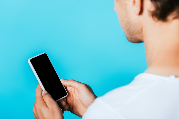 Widok na młodego człowieka trzymającego smartfona z pustym ekranem odizolowanym na niebiesko  - Zdjęcie, obraz
